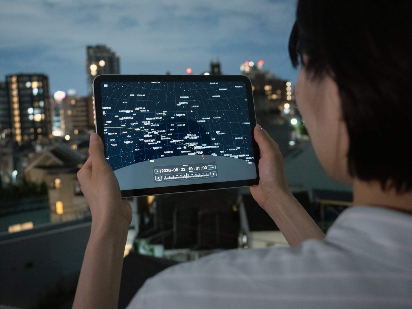 夜のベランダでタブレットにステラナビゲータ・モバイルの星図を表示し、彗星の位置を確認している様子
